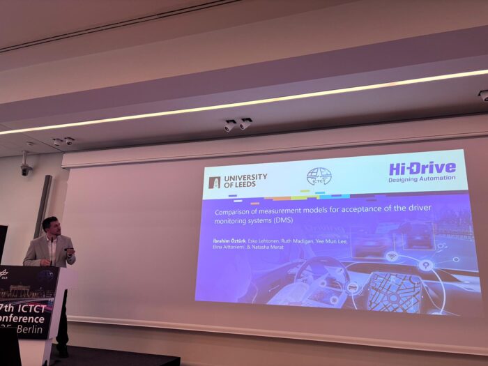 Ibrahim Ozturk presenting standing at a podium infront of a screen with a title slide of her presentation